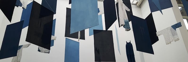 Photo von blauen und schwarzen quadratischen Platten und weißen Oberteilen, die wie ein Mobile von der Decke hängen.
